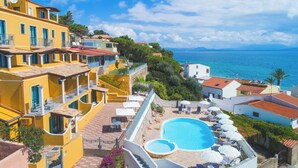 A coastal hotel with a pool, balconies, and a view of the sea.