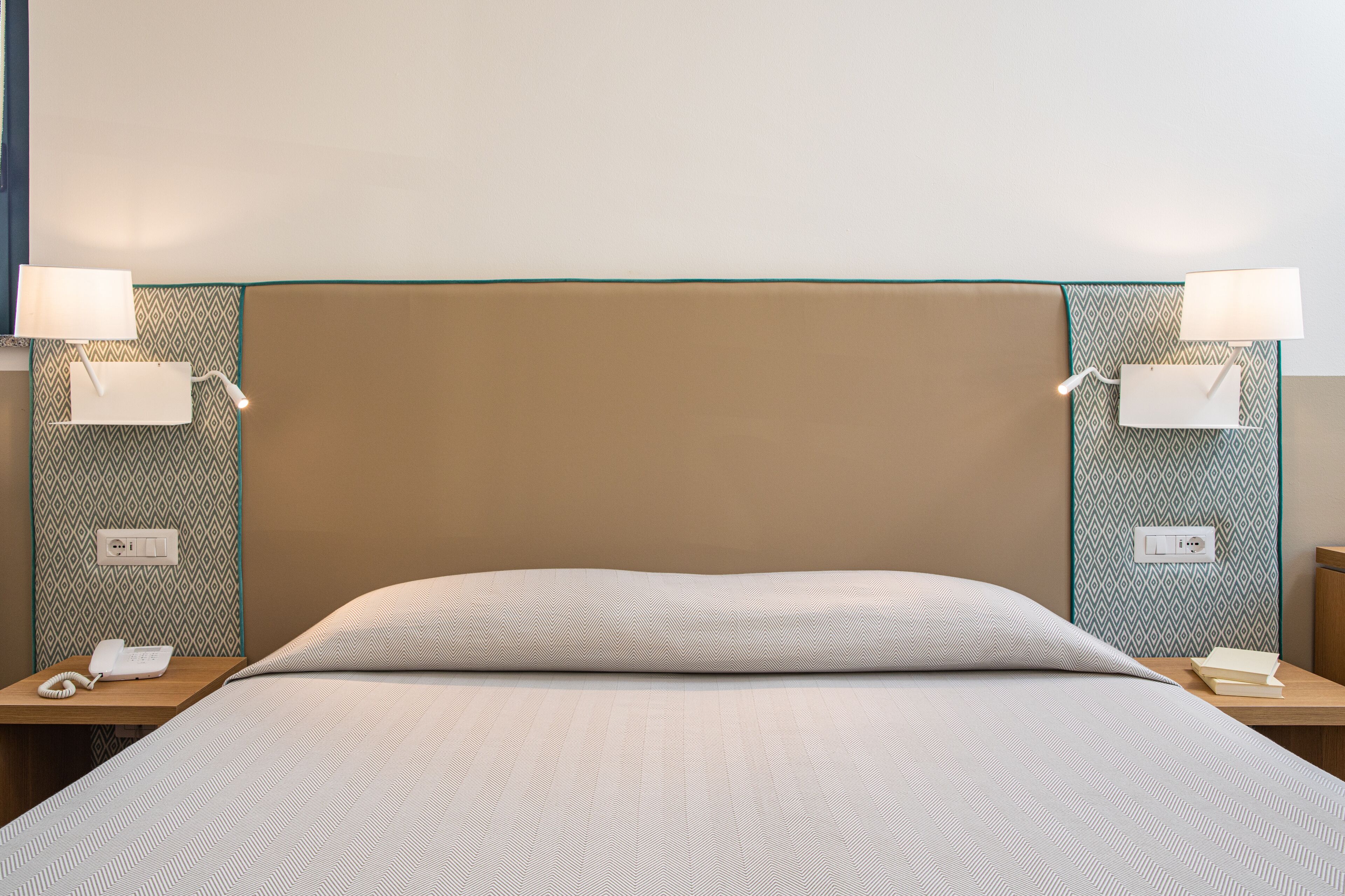 A neatly made bed with a striped bedspread, two bedside lamps, a telephone, and a patterned wall.