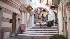 A narrow street with a stone archway leading to a building with a sign reading "ENOSIM".