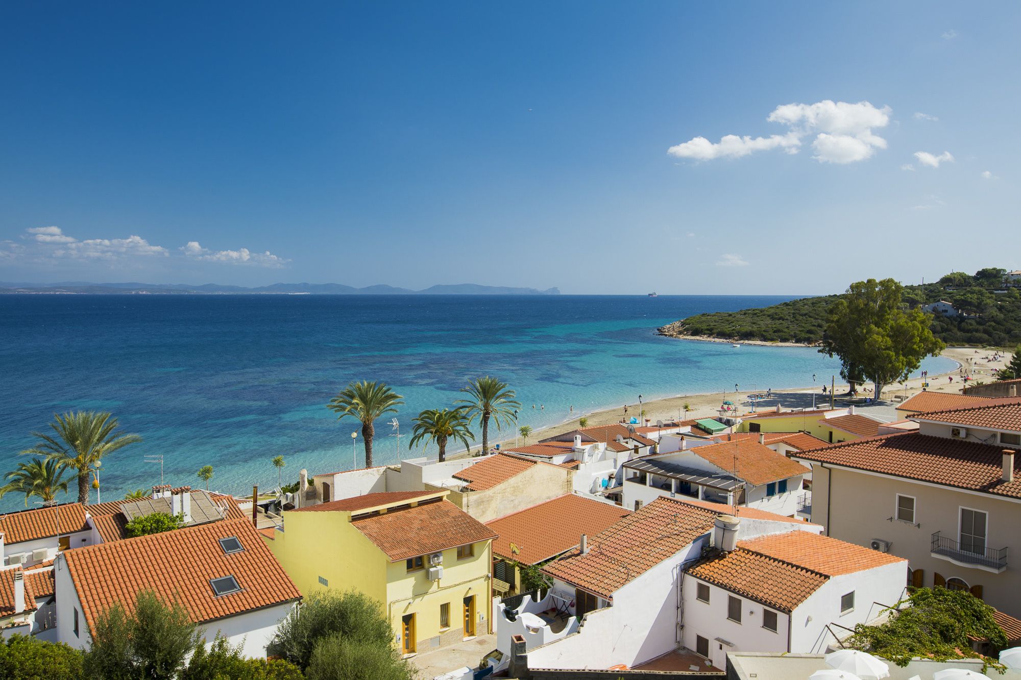 Un pueblo costero con edificios de tejas color terracota, una playa y aguas azules cristalinas.
