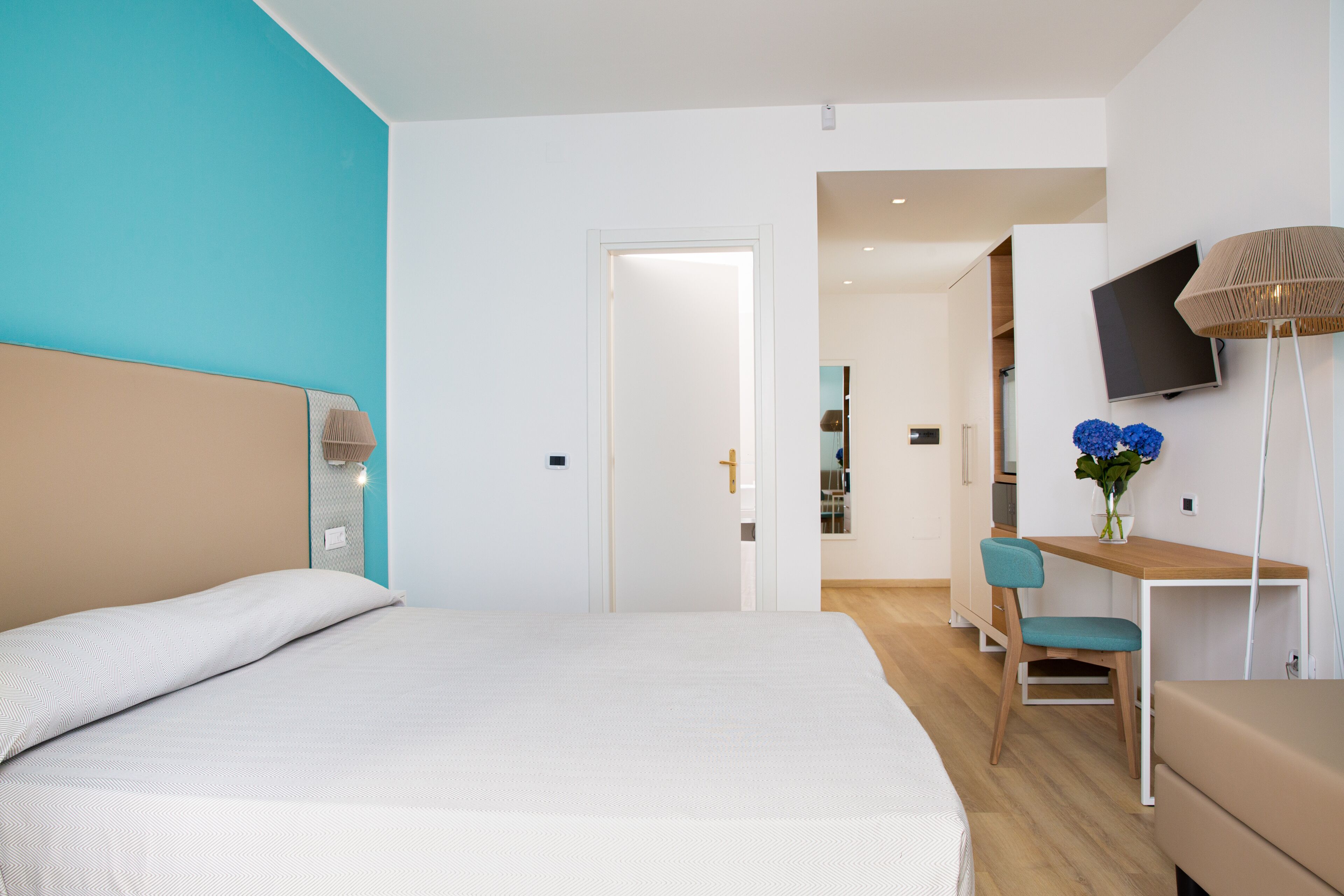 A modern hotel room with a large bed, a desk with a chair, and a TV mounted on the wall.