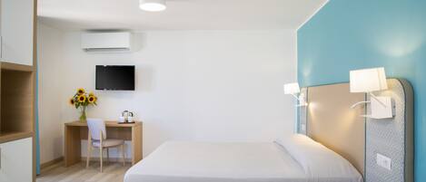 A hotel room with a bed, a desk with a chair, a TV, and a wall-mounted lamp.