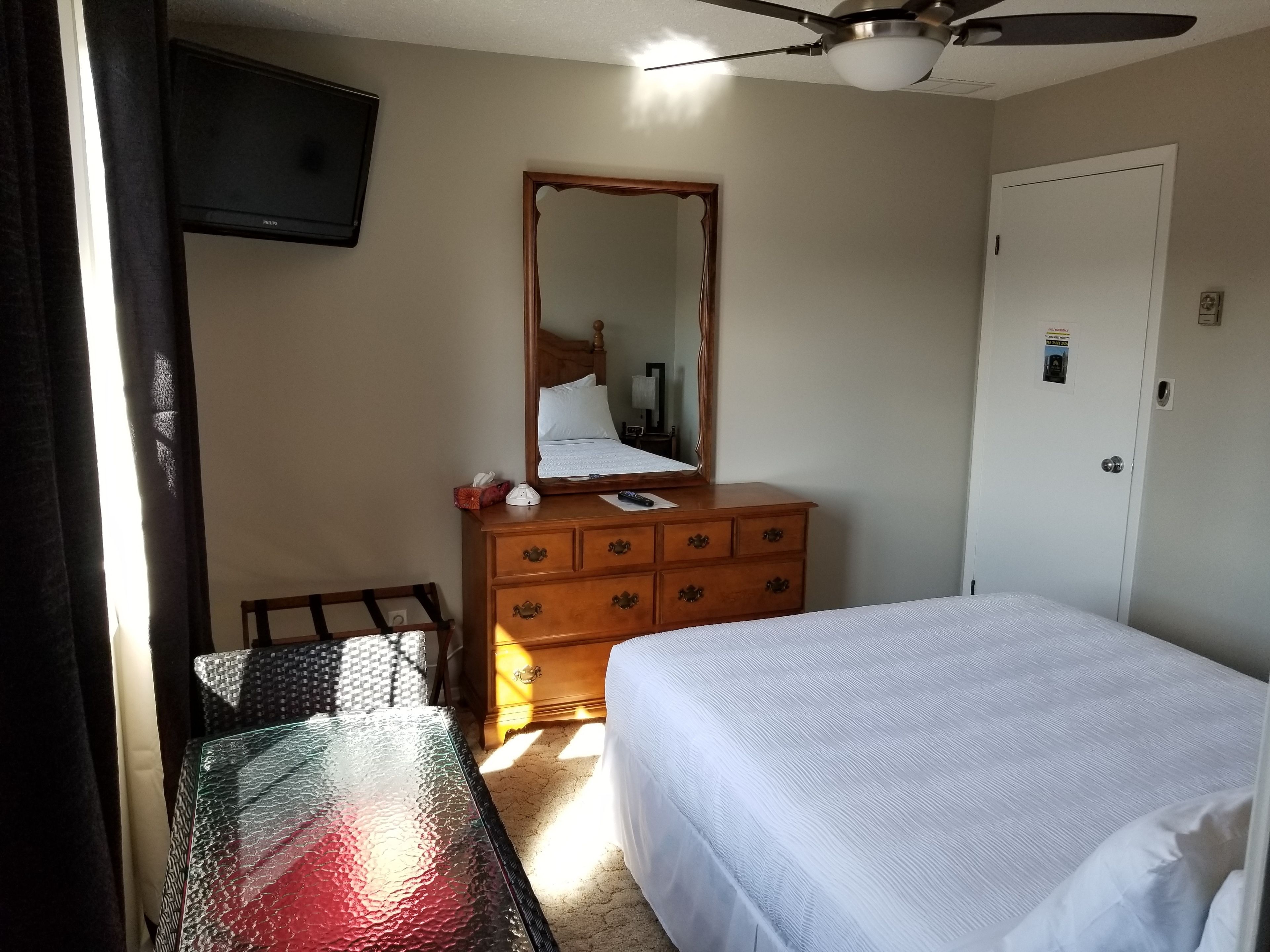 A hotel room with a bed, a dresser, a mirror, a television, and a table.