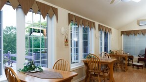 A dining area with wooden tables and chairs, large windows with curtains, and a view of the outdoors. - Bee 'n Bee Bed n' Breakfast (Lambton Shores)