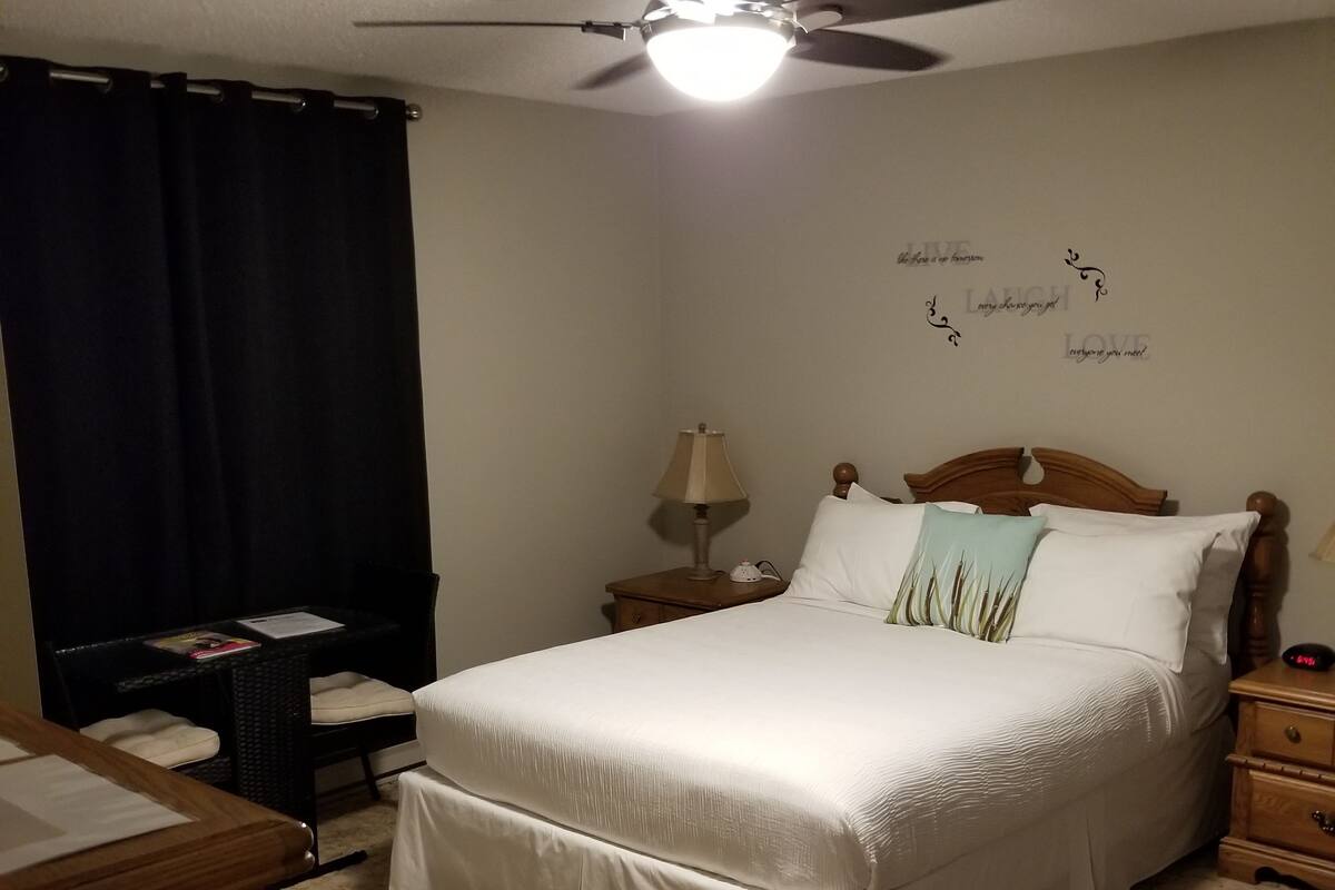 Een keurig opgeruimde slaapkamer met een bed, nachtkastjes, een bureau en een plafondventilator.