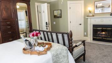 A bedroom with a bed, a wooden chair, a fireplace, and a door.