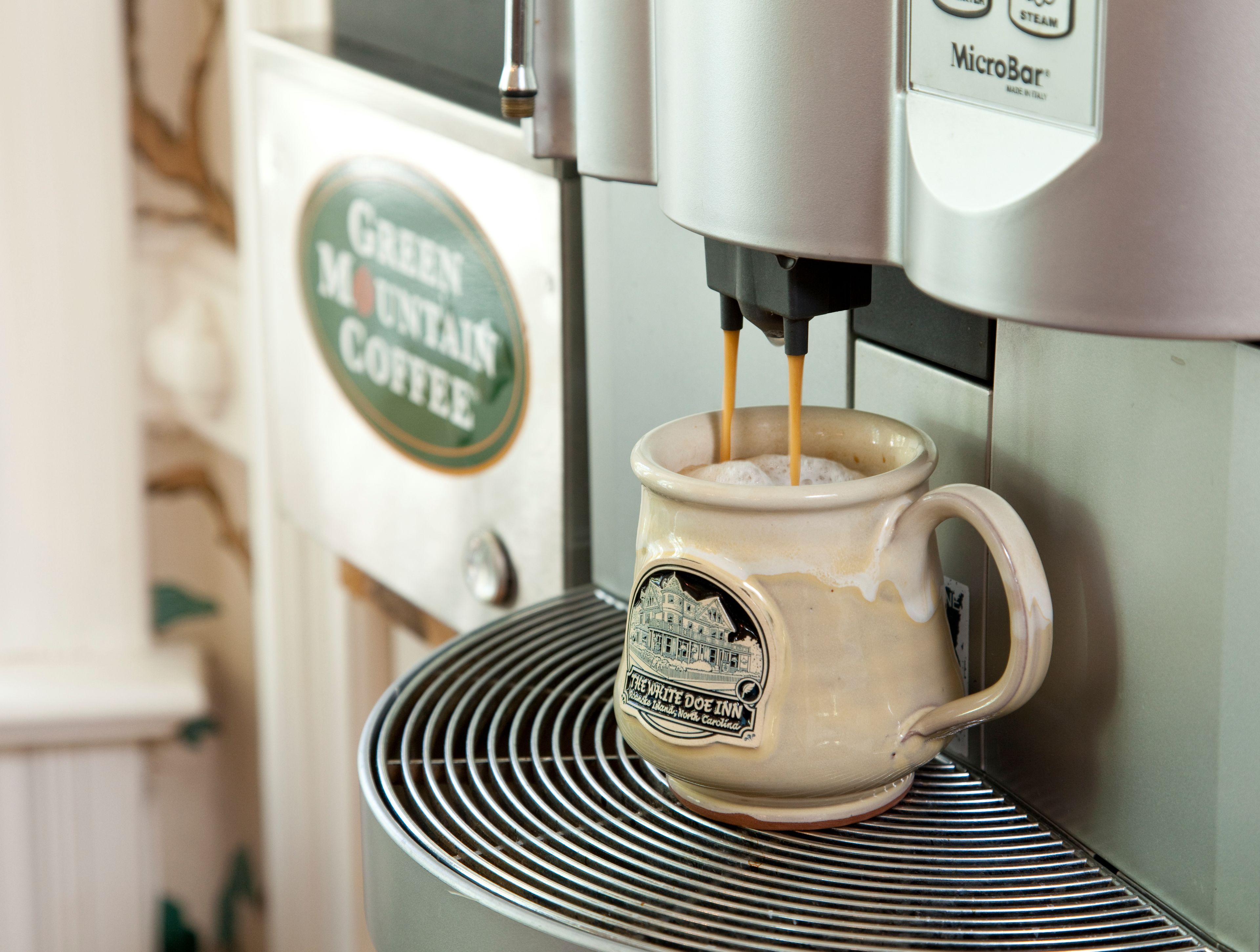 A coffee machine dispensing coffee into a mug with a label that reads "The White Doe Inn".
