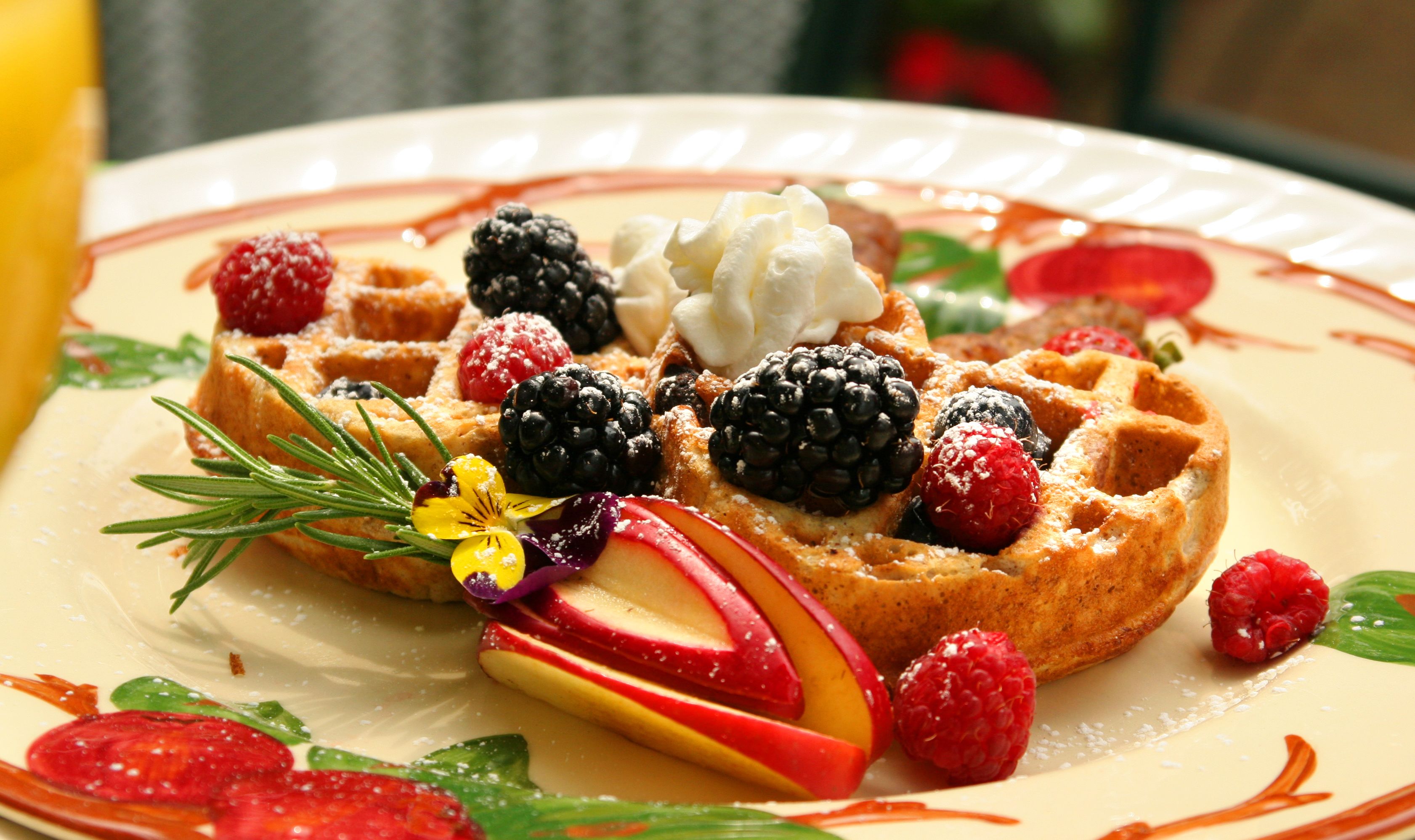 A plate with a waffle topped with whipped cream, berries, and a sprig of rosemary.