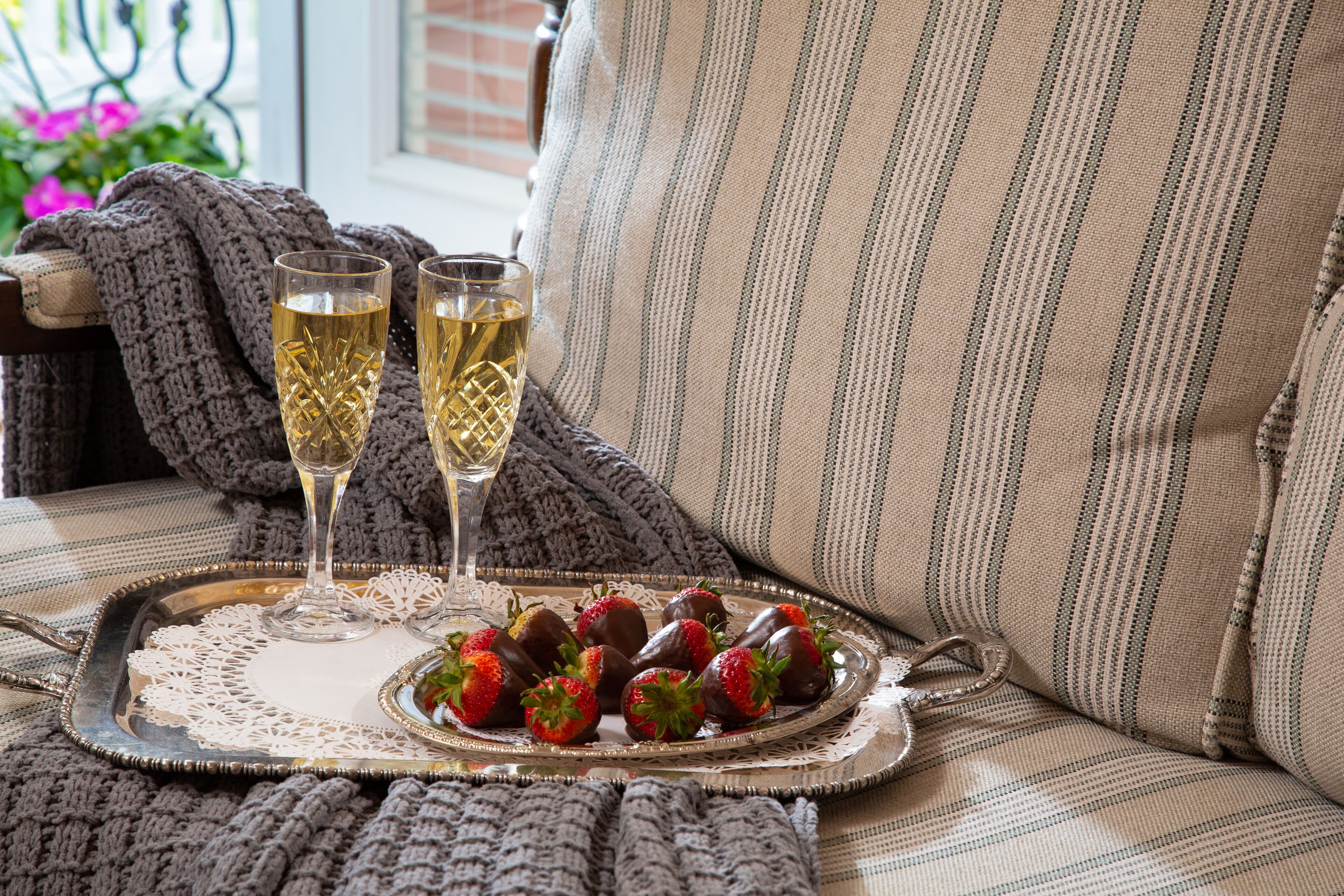 A tray with chocolate-covered strawberries and two glasses of champagne on a cushioned surface.
