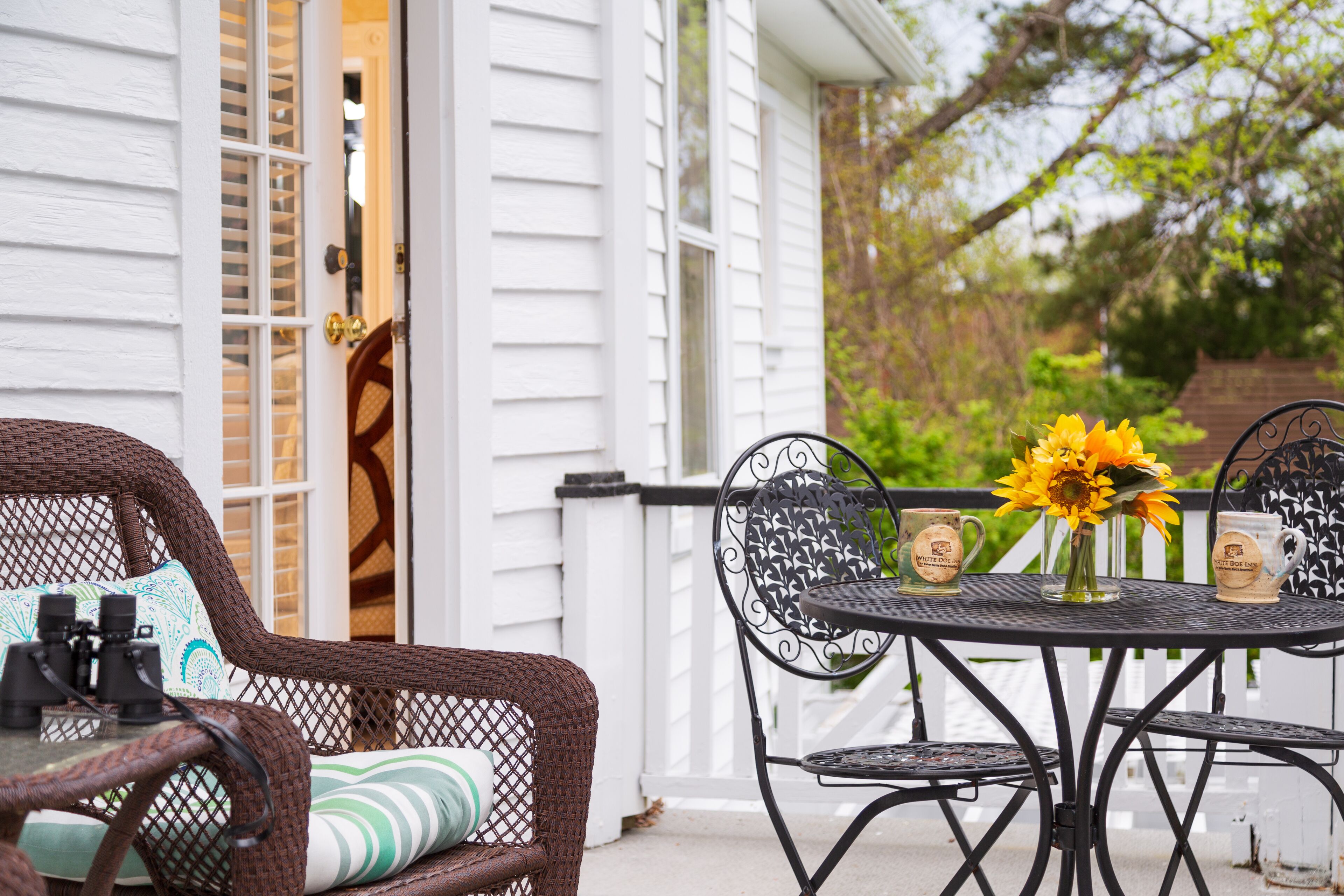A patio with wicker furniture, a round metal table, and a vase with sunflowers.