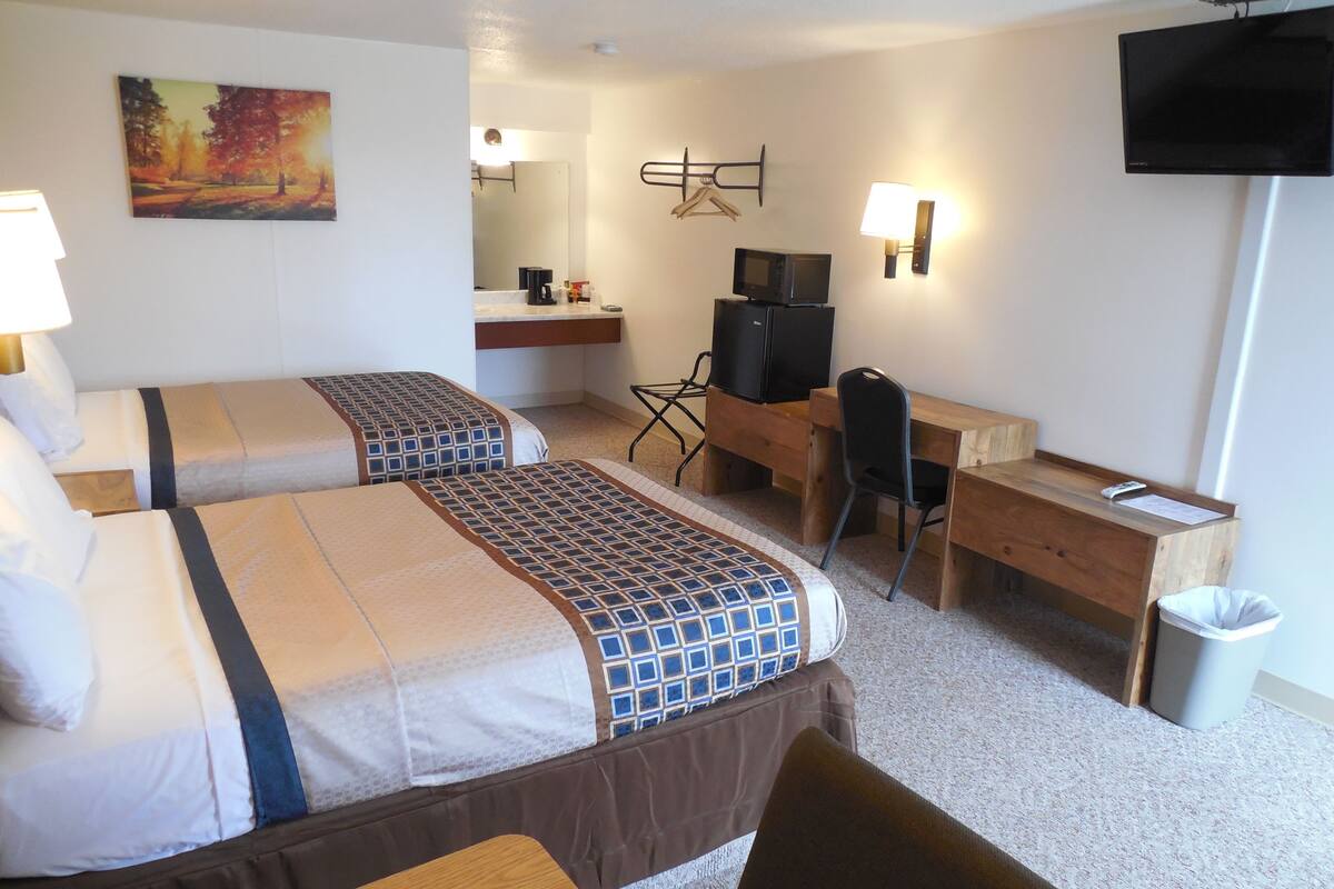 A hotel room with two beds, a desk, a chair, a TV, and a trash bin.