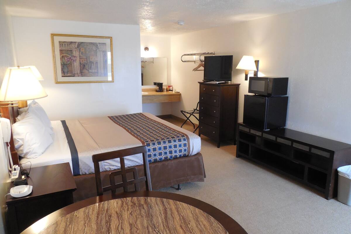 A hotel room with a bed, a desk with a lamp, a television, a dresser, and a painting on the wall.