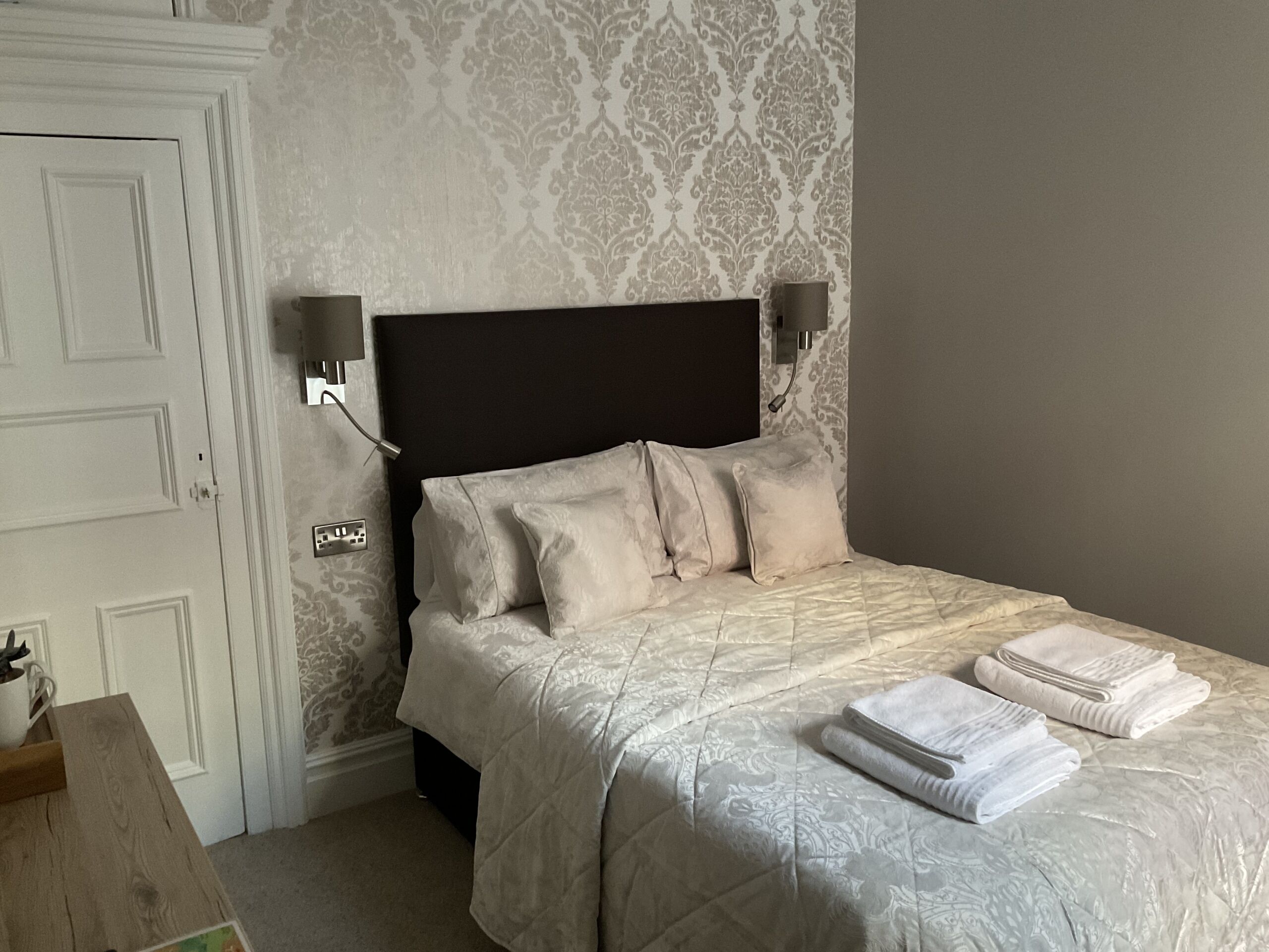 Quarto com cama, luminárias de cabeceira, mesa de cabeceira e porta.