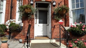 A brick building with a white door, two hanging flower baskets, and a red sign. - Glenora Guest House (Whitby)