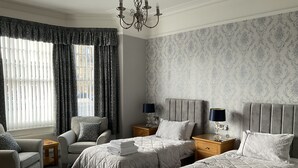 A hotel room with two beds, a sofa, a chandelier, and patterned wallpaper. - Glenora Guest House (Whitby)