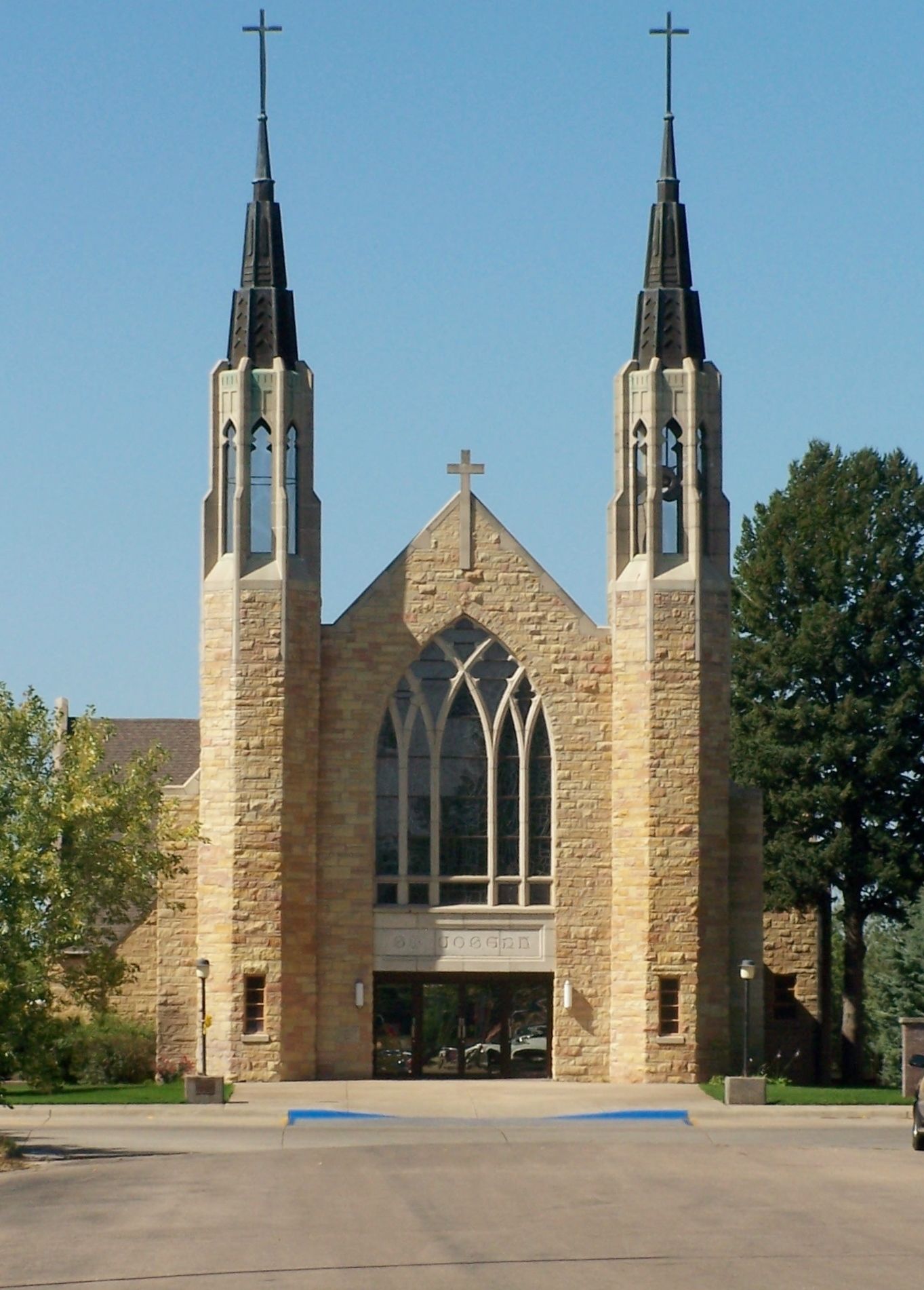 Une église dotée de deux tours, d’une grande fenêtre en arc de cercle et d’une croix au sommet.