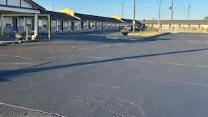 A motel with a row of single-story buildings, a parking lot, and a clear blue sky. - Interstate Inn Express (Tulsa)