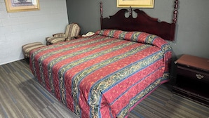 A neatly arranged hotel room with a large bed, a chair, a bedside table, and a framed picture on the wall. - Interstate Inn Express (Tulsa)