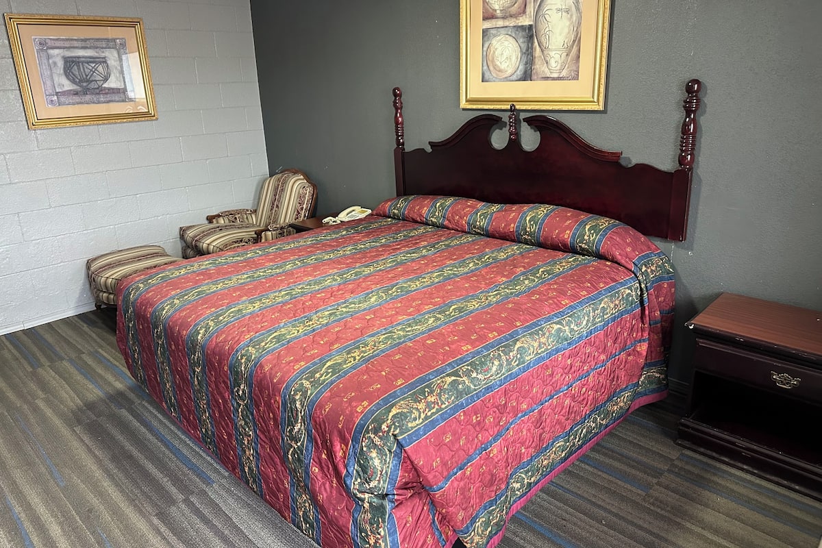 Camera d'albergo ben ordinata con un letto grande, una sedia, un comodino e un quadro incorniciato appeso al muro.