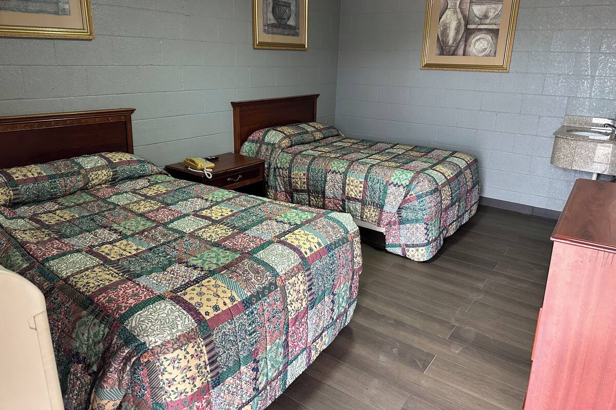 Una stanza con due letti, ognuno con una coperta a motivi decorativi, un comodino in legno con il telefono e quadri appesi alle pareti.