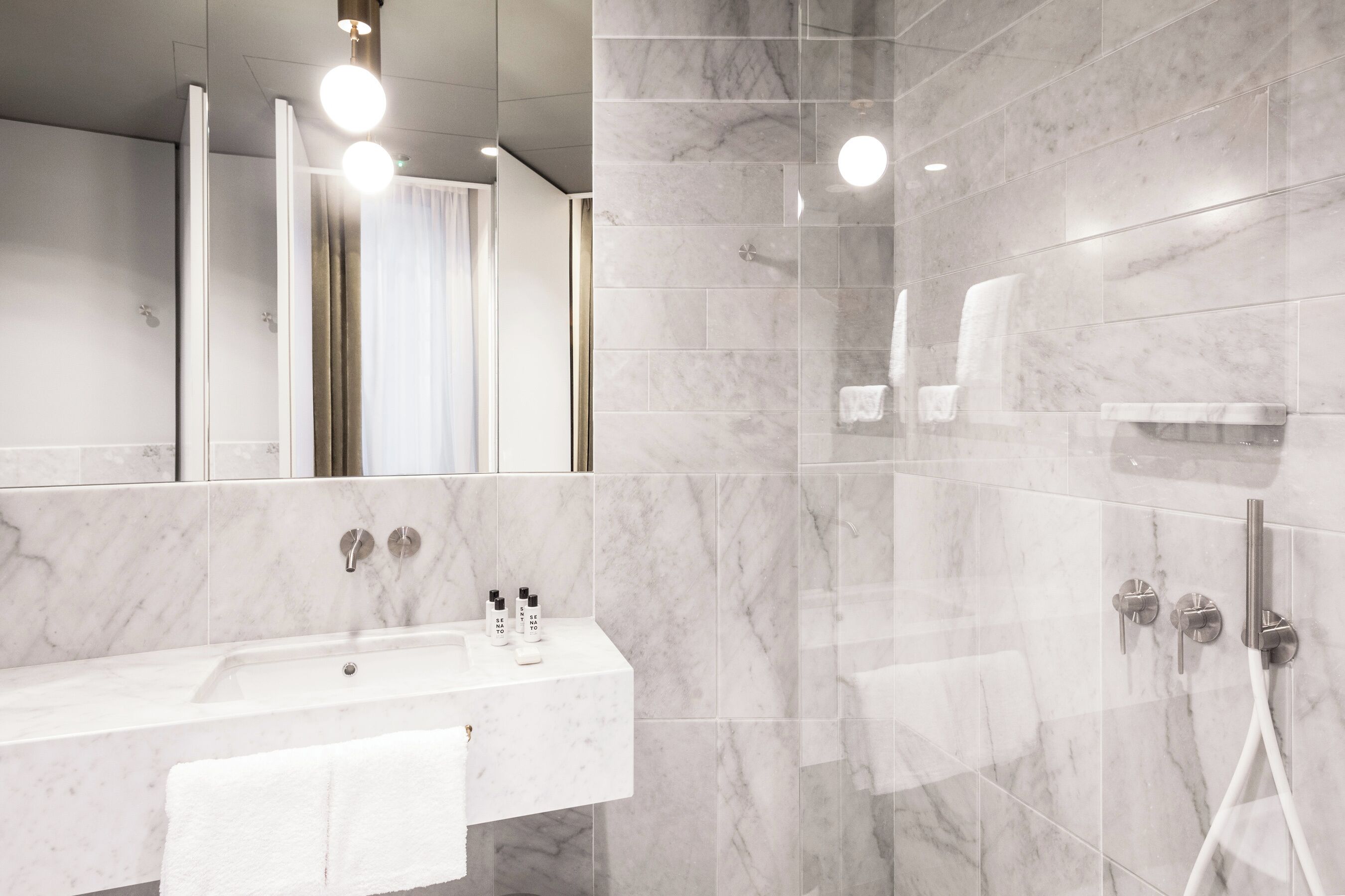 A modern bathroom with a marble sink, a large mirror, and a glass-enclosed shower area.