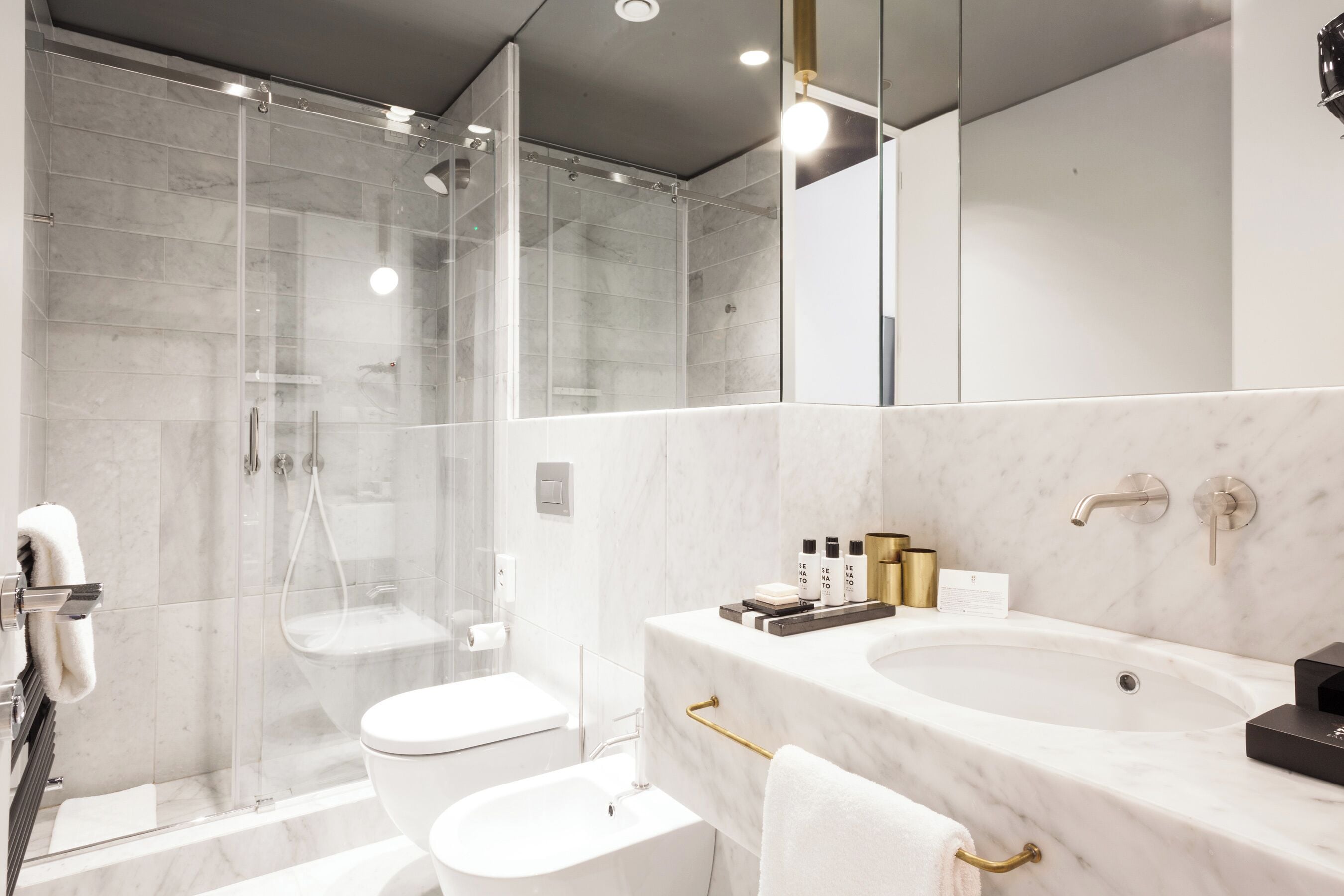Un bagno moderno con doccia vetrata, un WC bianco e un lavabo in marmo con dettagli dorati.