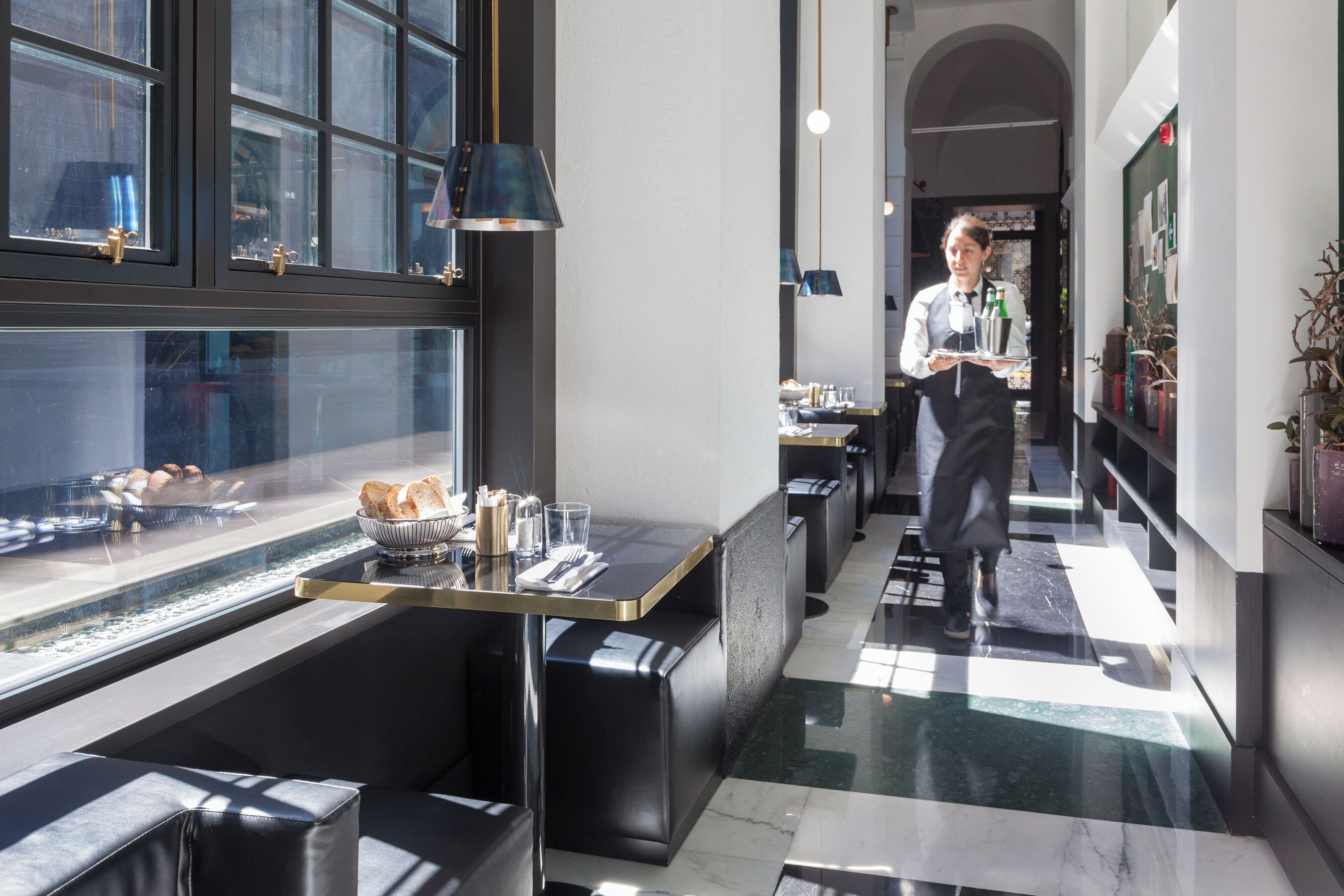 Un hall d’hôtel moderne doté d’un espace salon, d’un comptoir d’accueil et offrant une vue sur la rue grâce à de grandes fenêtres.