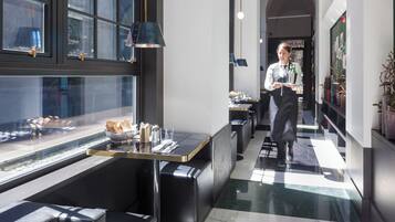 Un hall d’hôtel moderne doté d’un espace salon, d’un comptoir d’accueil et offrant une vue sur la rue grâce à de grandes fenêtres.
