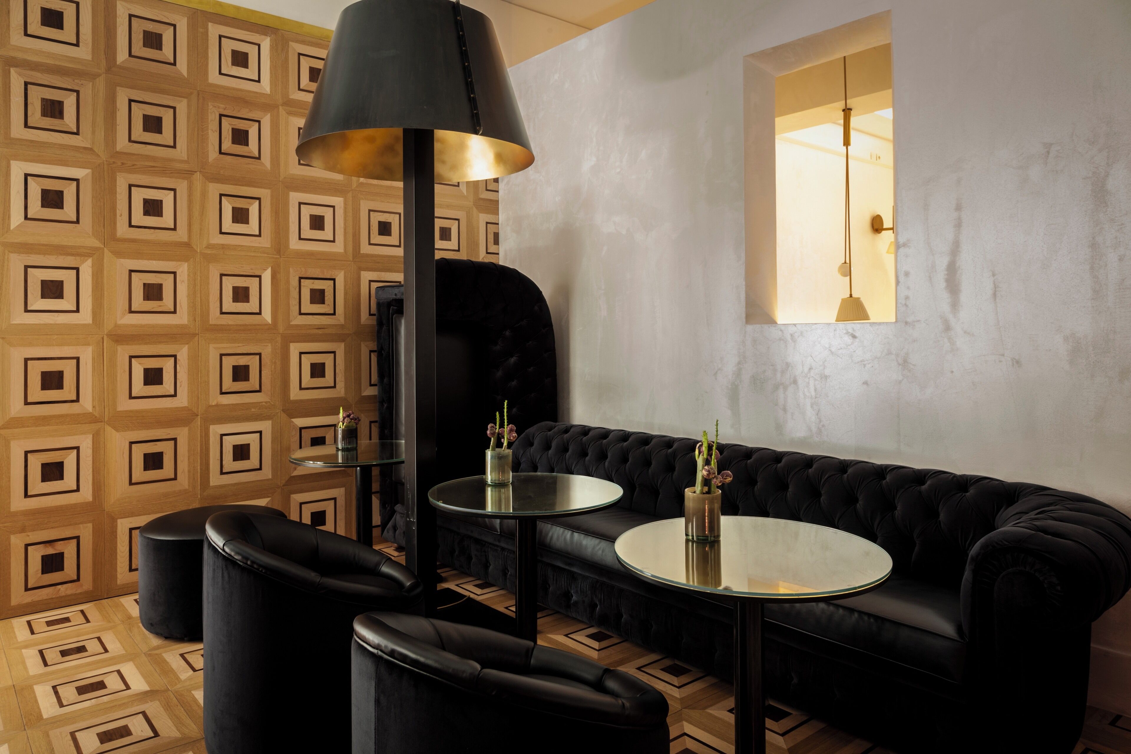 A modern interior with a black leather sofa, two round tables, and a large floor lamp.