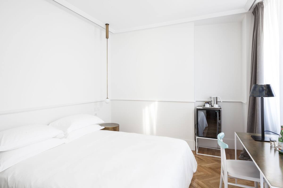 Habitació d'hotel amb un llit gran, una taula de treball amb una cadira, una l àmpada i un petit armari.