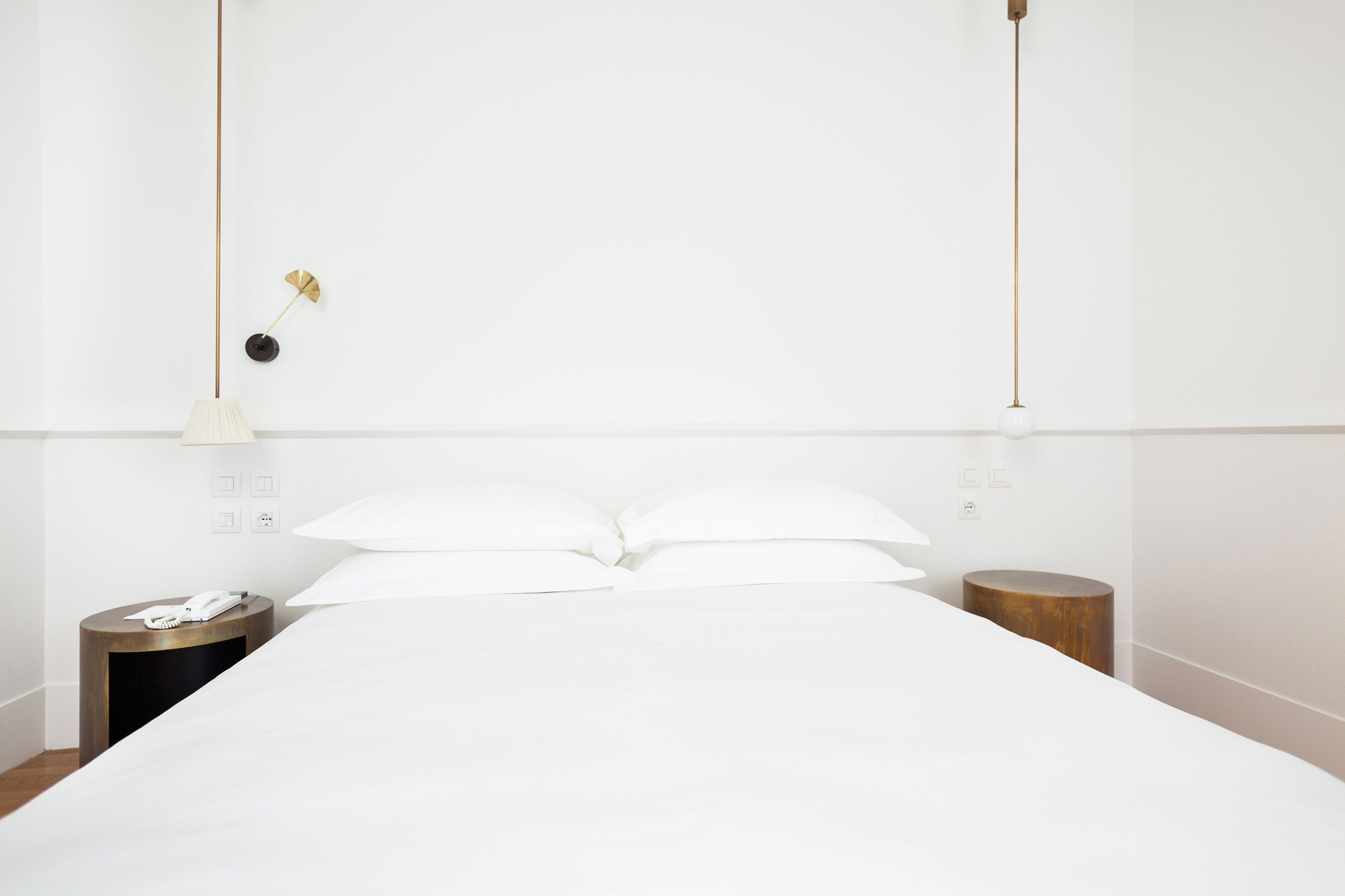 A neatly made bed with white linens, a bedside table with a lamp, and a small wooden stool.