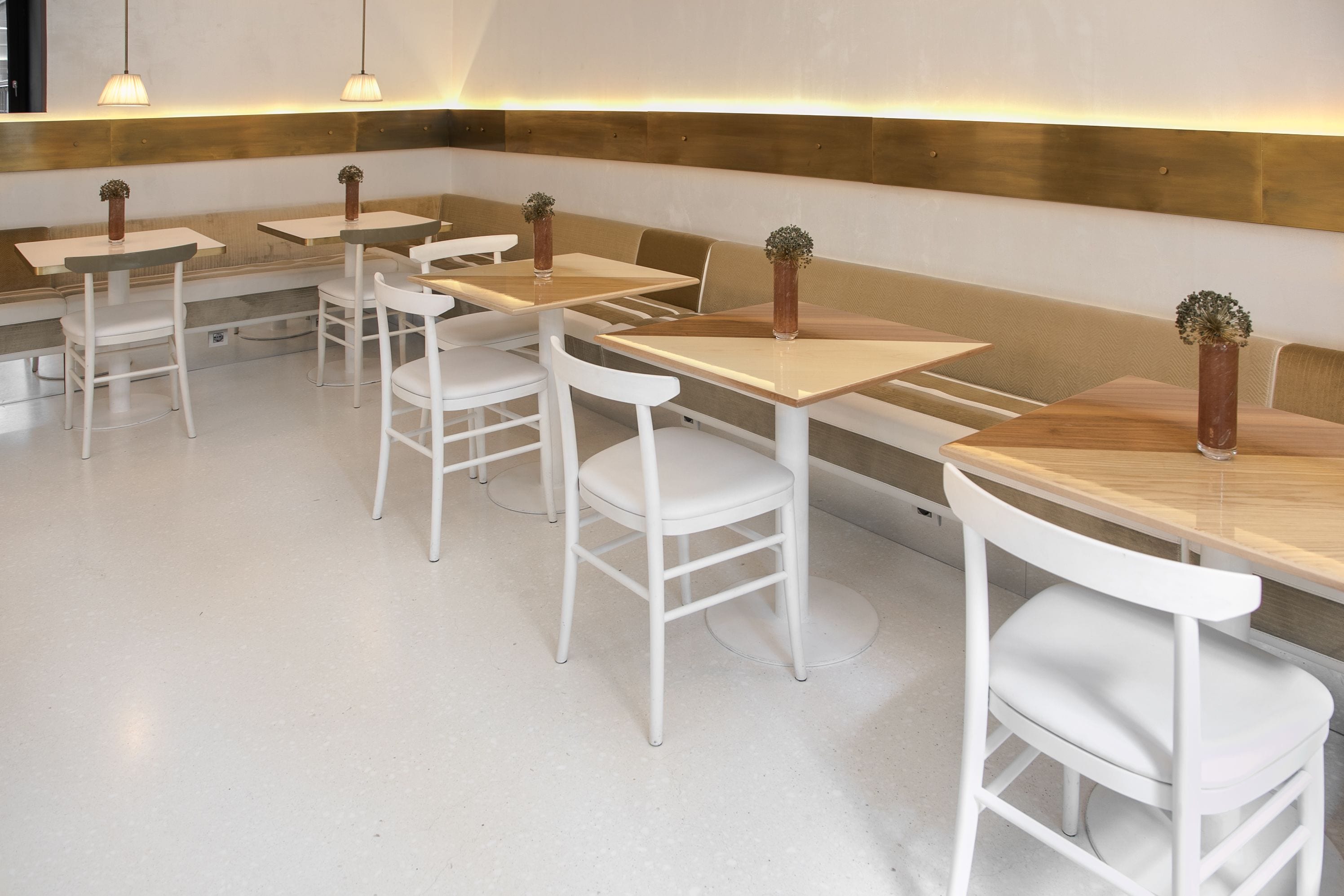 Zona pranzo moderna con sedie e tavoli bianchi, panche in legno e lampade a sospensione.