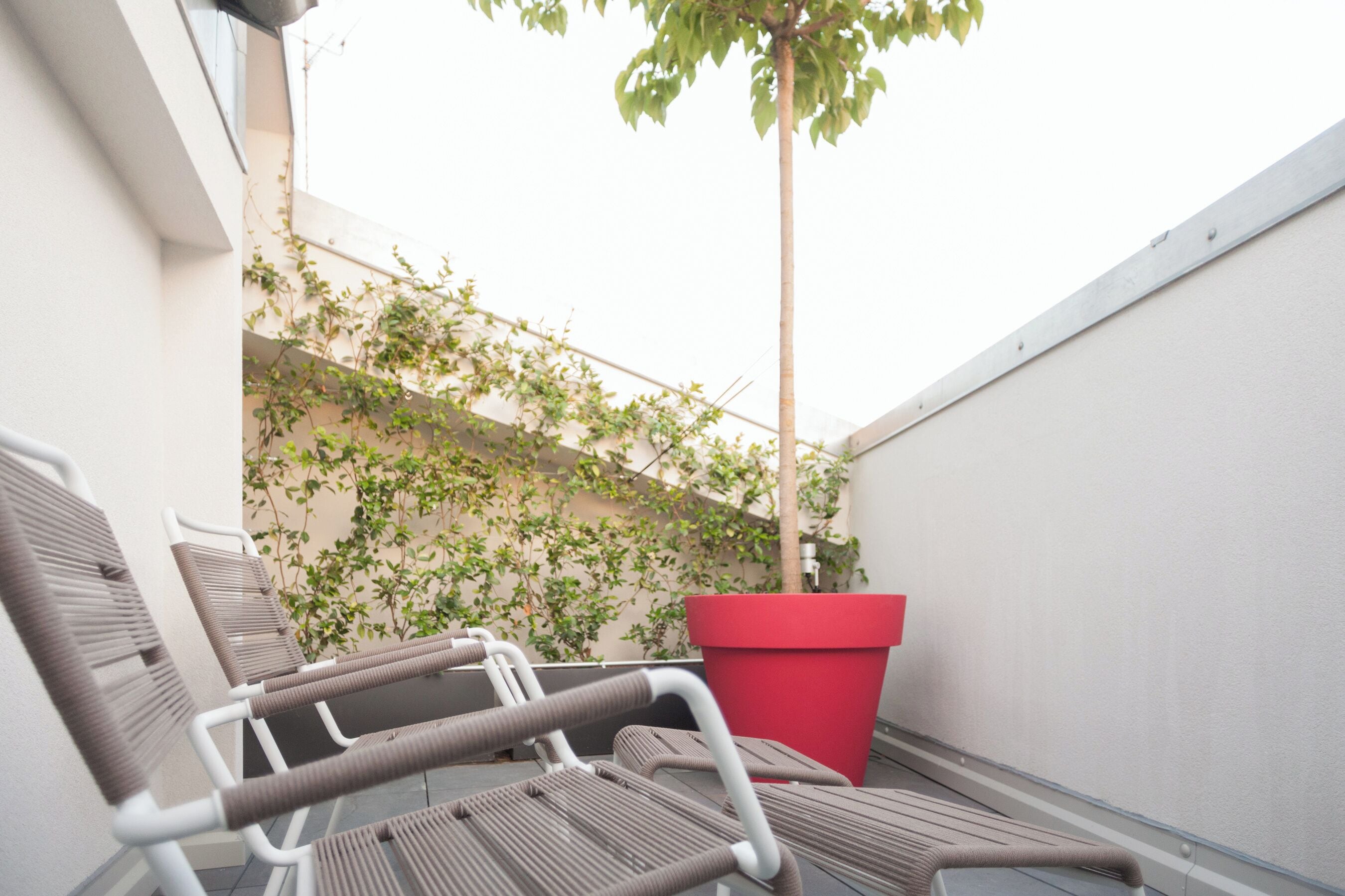 Un petit espace extérieur aménagé avec quelques chaises et un jardinier rouge.
