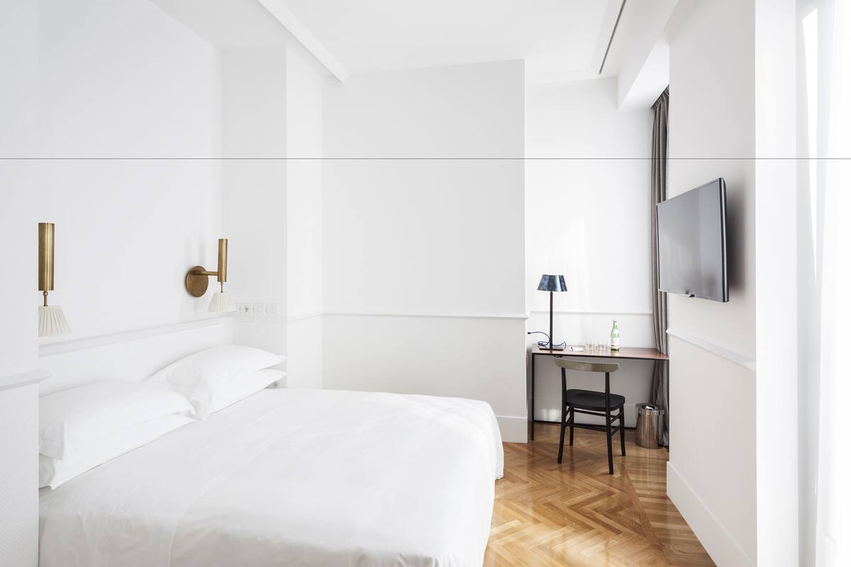 Una habitació d'hotel moderna amb un llit gran, un escriptori amb una cadira, una televisió penjada a la paret i una taula petita amb una làmpada.