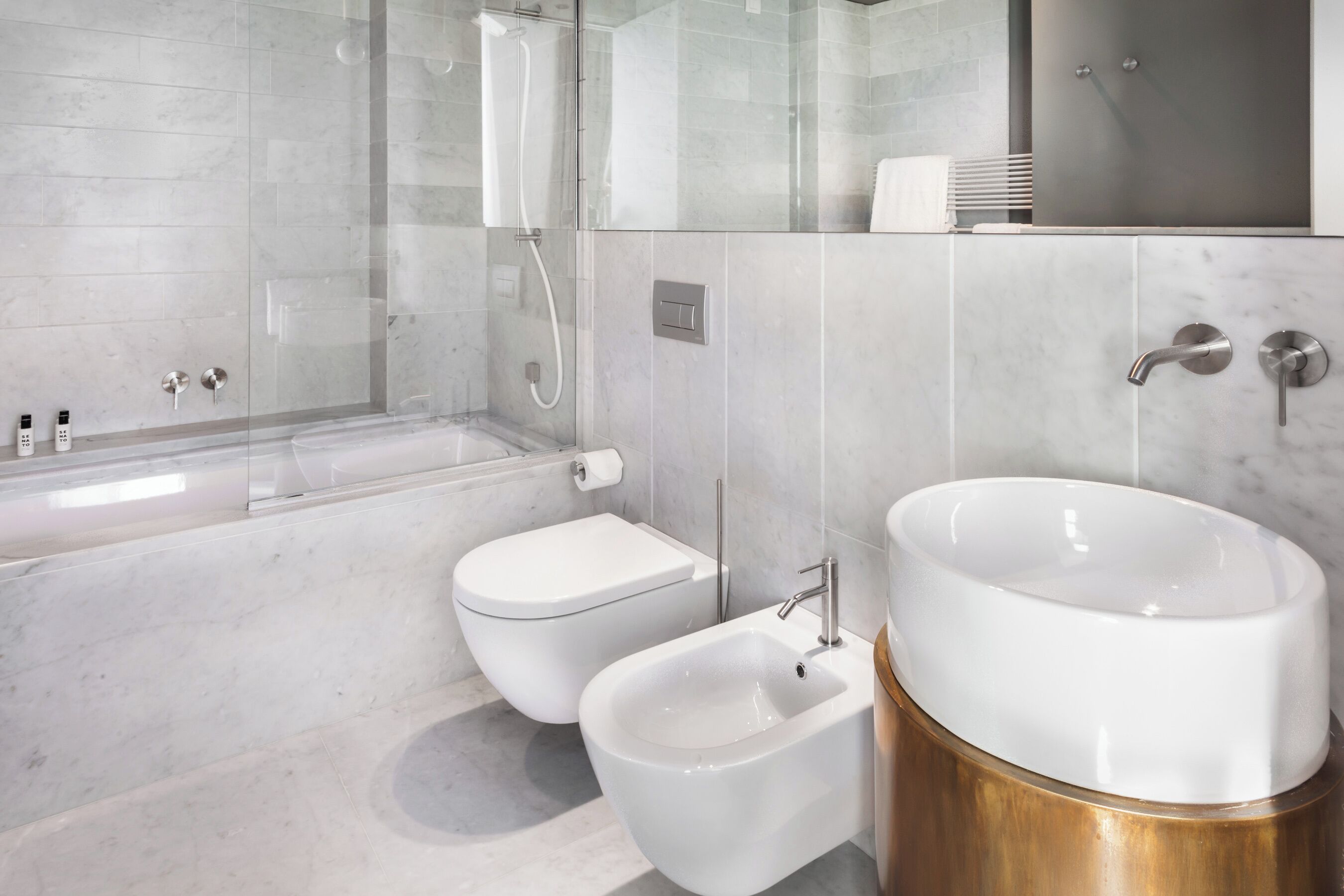 Une salle de bain moderne dotée d’une douche à parois de verre, d’une baignoire sur pieds, d’un bidet et d’un grand lavabo avec un socle doré.