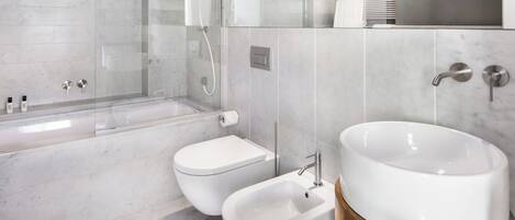 Une salle de bain moderne dotée d’une douche à parois de verre, d’une baignoire sur pieds, d’un bidet et d’un grand lavabo avec un socle doré.