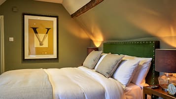 Una cama bien hecha con cabecera verde, una obra de arte enmarcada en la pared y una mesita de noche con lámpara y reloj.