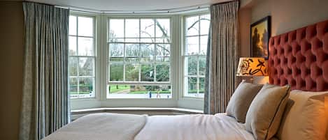 A bedroom with a large bed, a window with curtains, a red headboard, and a lamp on the nightstand.
