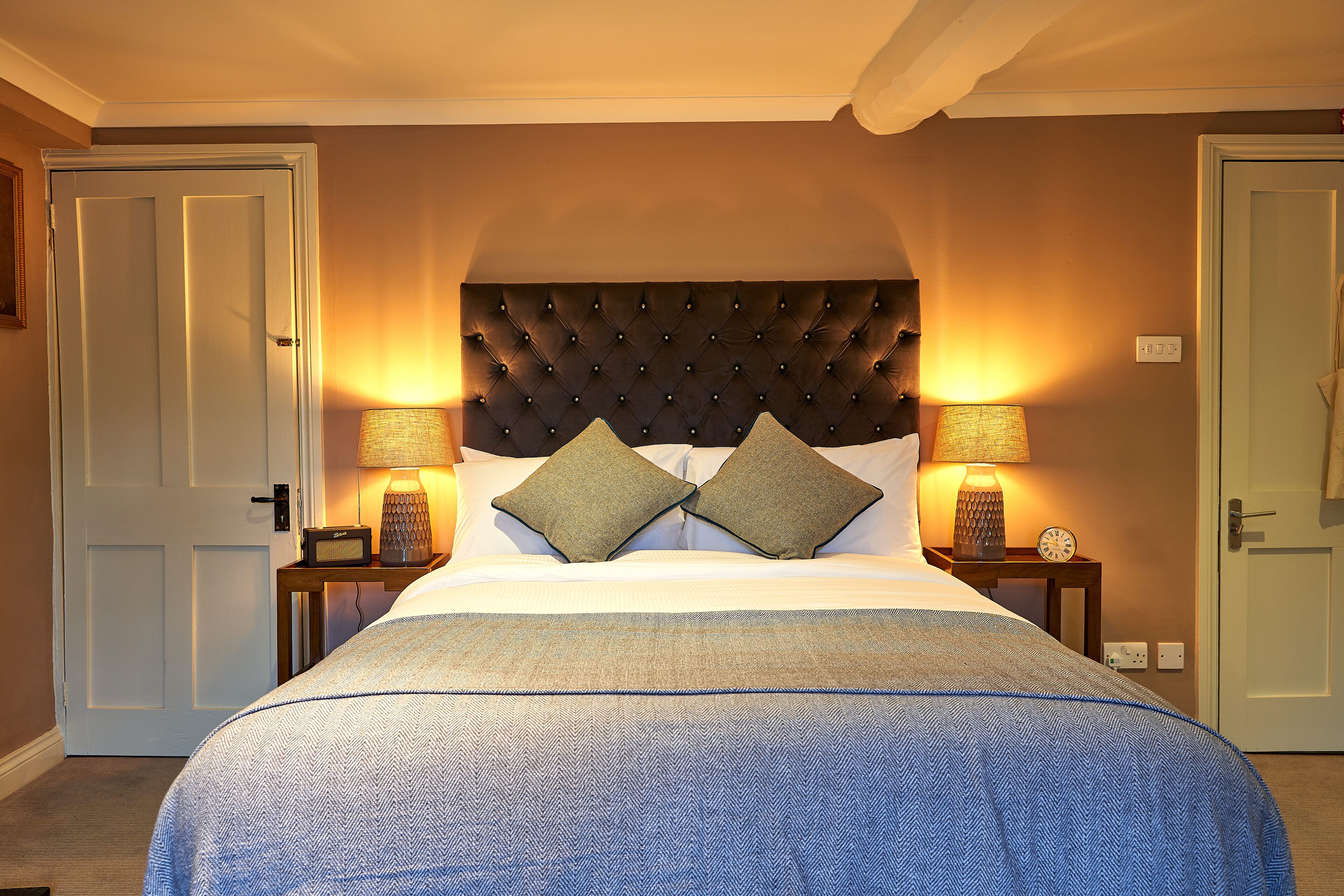 A neatly made bed with a tufted headboard, two bedside lamps, and a small table with a clock.