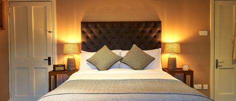 A neatly made bed with a tufted headboard, two bedside lamps, and a small table with a clock.