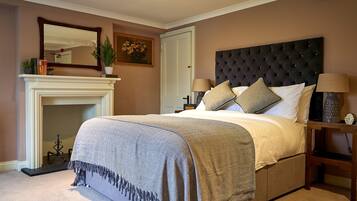 A bedroom with a large bed, a fireplace, a nightstand, and a mirror on the wall.