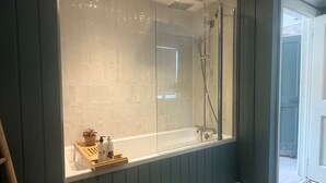 Un baño con ducha vidriada, bañera y suelo de baldosas.