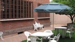Edificio de ladrillo con grandes ventanales y un patio con muebles de plástico blanco y una sombrilla.