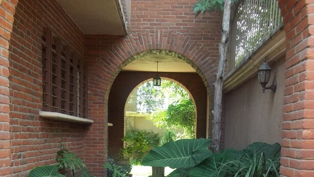 Un edificio de ladrillo con un patio empedrado, plantas grandes en macetas y una entrada en arco.