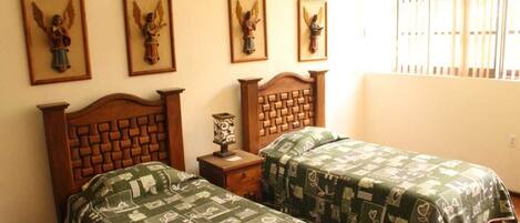 A bedroom with two beds, a wooden headboard, a nightstand, and four framed angel pictures on the wall.