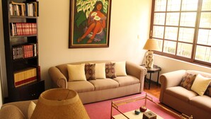 Una sala de estar con un sofá color beige, una estantería, un cuadro, una lámpara y una mesita con adornos.