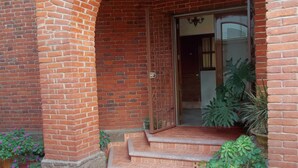 Una entrada de ladrillo con puerta de cristal y escalones que la llevan a ella, con plantas en macetas alrededor.