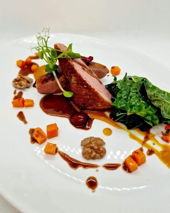 Un plato blanco con guarnición de carne cortada, verduras y salsa.
