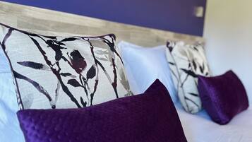A bed with a purple pillow and a floral-patterned pillow, a wooden headboard, and a wall with floral artwork.