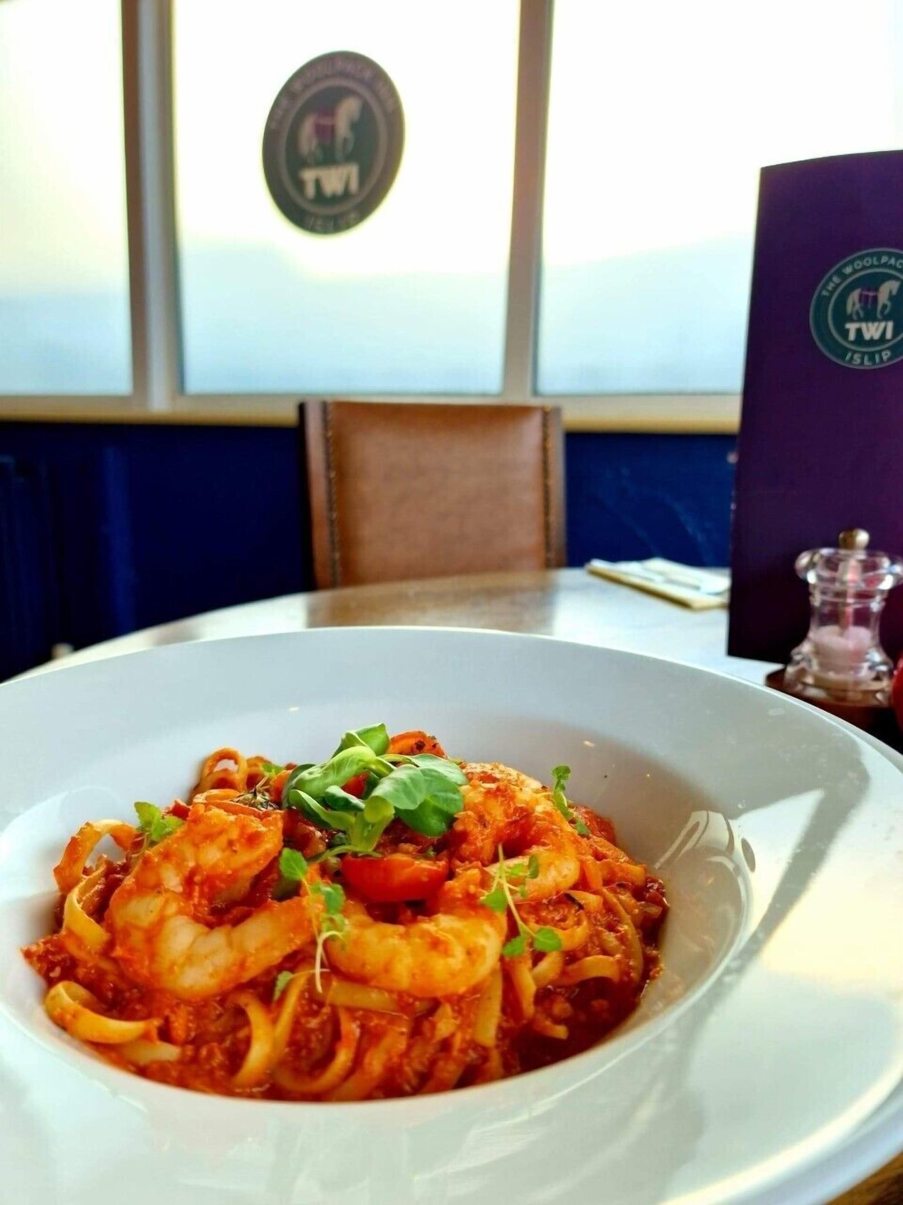 Un piatto di pasta con frutti di mare su un piatto bianco, con un menu e un logo sul tavolo.